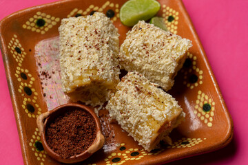 Mexican corn on the cob also called elotes with cheese and mayonnaise on pink background