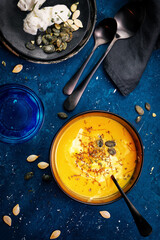 Vegetarian autumn pumpkin cream soup with seeds and cream over dark blue background