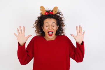 Emotive Young arab woman with curly hair wearing christmas hea laughs loudly, hears funny joke or story, raises palms with satisfaction, being overjoyed, amused by friend. People and emotions concept.
