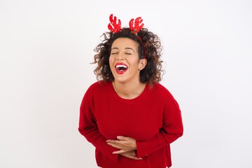 Young arab woman with curly hair wearing christmas headband standing on white background smiling and laughing hard out loud because funny crazy joke with hands on body.