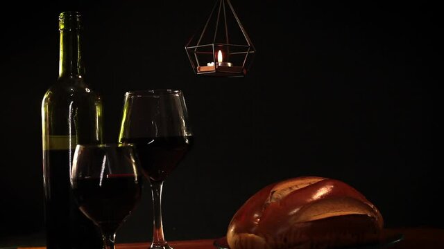 Garrafa de vinho, 2 ta&ccedil;as, p&atilde;o caseiro, vela no alto da bancada de madeira, com fundo escuro, contornos claros e reflexo de brilhos nos vidros.
