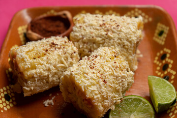 Mexican corn on the cob also called elotes with cheese and mayonnaise on pink background