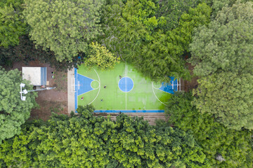 Vista aérea cenital sobre una cancha de basketball, rodeada por árboles, con cuatro personas...