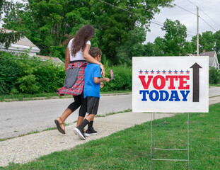 African American Mother walking to vote at Polling Station with Arm Around Mixed Race Son waving a...