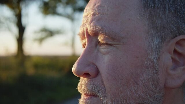 Close up of attractive elderly man face and beautiful green eyes looking forward outdoor enjoying sun shine. Senior citizen looks into the distance. Macro. Thoughtful look. True feelings. Grandfather.