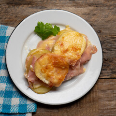 Scalloped potatoes with ham and cheese on wooden background