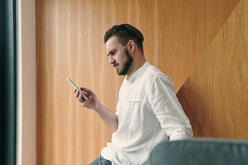 Portrait of focused young businessman holding smart phone and looking at screen