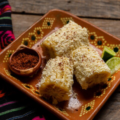 Mexican corn on the cob also called elotes with cheese and mayonnaise on wooden background
