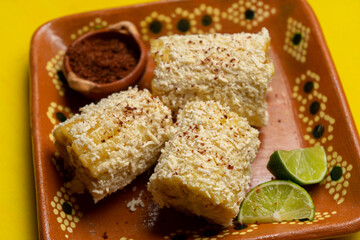 Mexican corn on the cob also called elotes with cheese and mayonnaise on yellow background