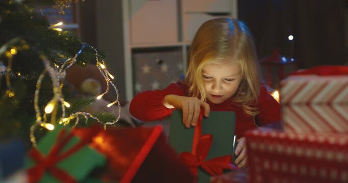 Close up of the beautiful small kid opening a box and looking at the x-mas present from Danta Claus.