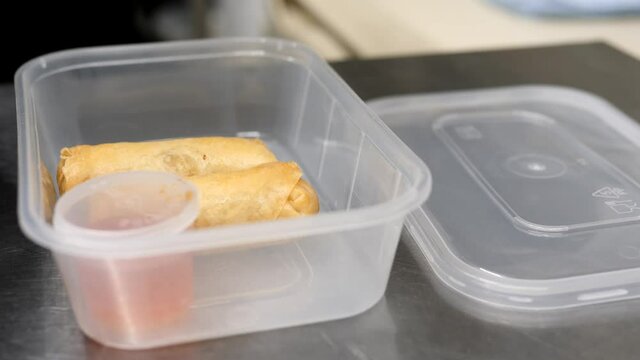 Woman chef put deep-fried vegetable spring roll with sweet chilli sauce into a takeaway box.