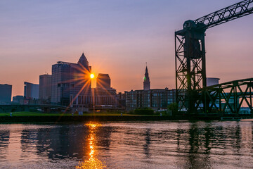 Industrial city on river at sunrise with sun between buildings