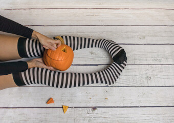 Woman in striped stockings preparing pumpkin for Halloween