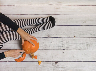 Woman in striped stockings preparing pumpkin for Halloween