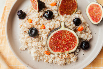 ripe juicy figs, blueberries and sea buckthorn berries in oatmeal porridge on flat porcelain plate, close-up, selective focus
