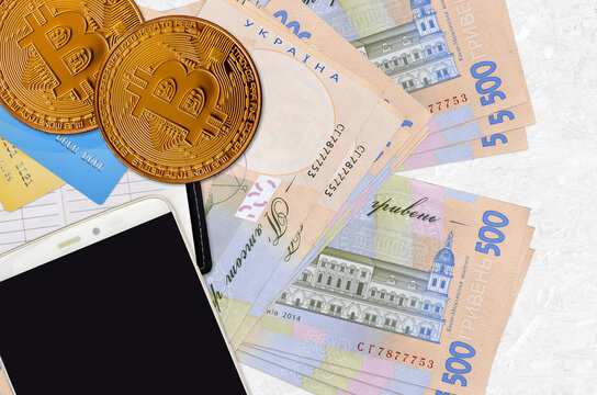 500 Ukrainian hryvnias bills and golden bitcoins with smartphone and credit cards. Cryptocurrency investment concept. Crypto mining or trading