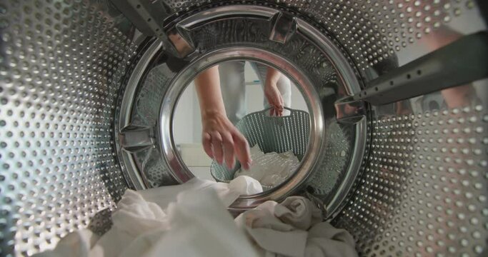 A woman puts white laundry in the washing machine
