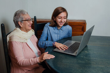 latin granddaughter teaching her grandmother something on the laptop in Mexican house