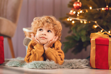 Cute little boy at home. Child sitting by the christmas gifts. Kid in a brown sweater.