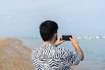 Adolescente con mascarilla haciendo fotos a los barcos que estan en el mar en la playa 