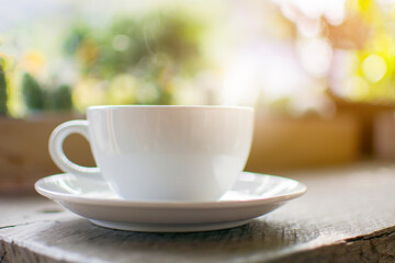 Fototapeta na wymiar A white cup of hot drink with steaming on the wooden table with bokeh of tree background