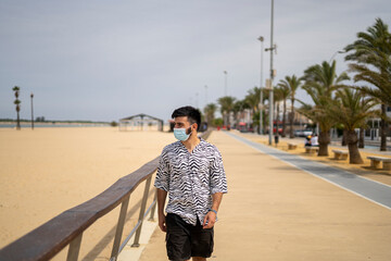 Hombre Joven con mascarilla paseando por el paseo marítimo disfrutando del mar y la playa