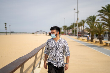 Hombre Joven con mascarilla paseando por el paseo marítimo disfrutando del mar y la playa