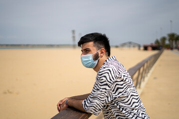 Hombre Joven con mascarilla paseando por el paseo marítimo disfrutando del mar y la playa