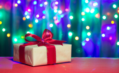 Christmas present box with red ribbon and bow on a background of multicolored bokeh