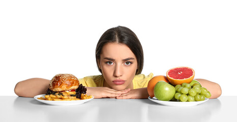 Woman choosing between fruits and burger with French fries on white background