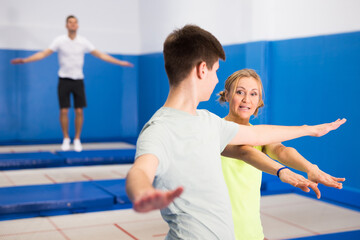 Obraz na płótnie Canvas Experienced female trampoline instructor teaching teenage boy of right technique in sports center..