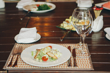 Selective focus Classical Caesar salad with roasted chiken, quail eggs, lettuce leaves, toasts, parmesan, tomatoes and cream sause on the white round plate close up on served table. Italian cuisine