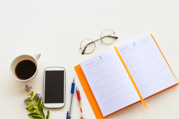 notebook planner ,mobile phone for business work with hot coffee espresso arrangement flat lay style at office on background white wooden