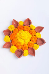 Flower Rangoli for Diwali Festival made using Marigold and leaf and Oil Lamp over white background,