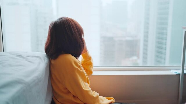 Asian woman sitting and looking outside after being locked down. Feeling lonely and homesick, concept stay home