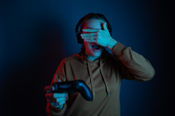 The gamer girl playing the online video game with joystick and headphones and close her eyes by the hand. Blue neon background. Gamer concept.