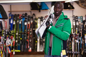 Fototapeta na wymiar Portrait of positive African American guy posing in skiing gear during shopping in sport goods store