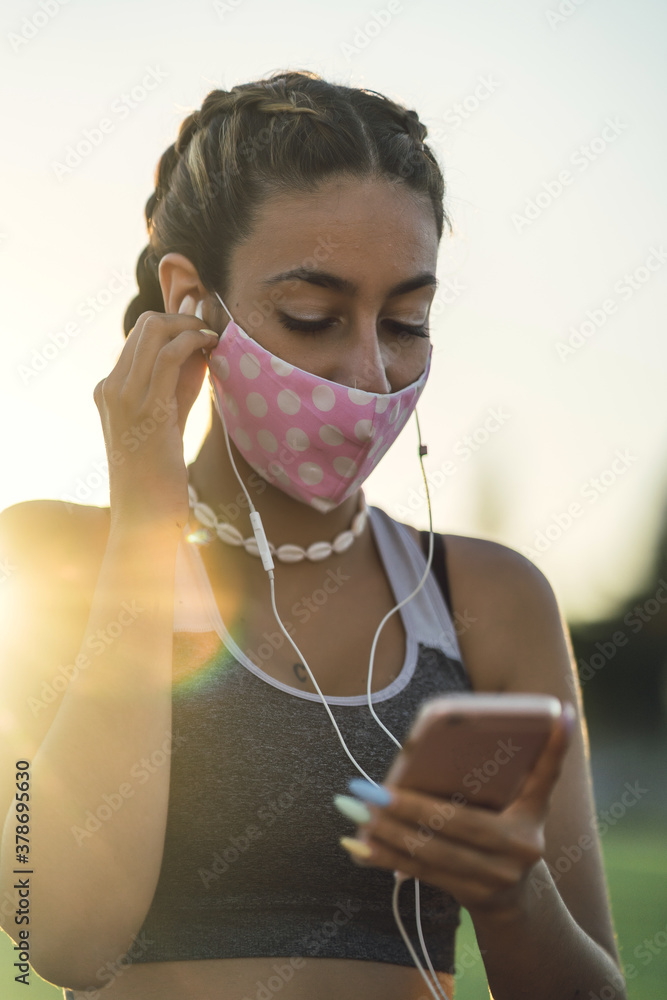 Poster Vertical shot of a woman listening to music on her phone while wearing a facemask