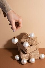 The girl's hand keeping the white christmas ball over the gift boxes. Light beige background. Photo with shadow. Holiday concept.