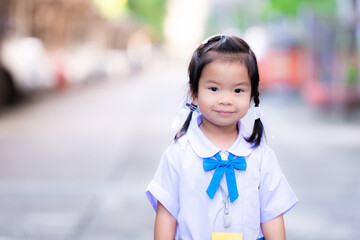 Student stood smiling sweetly looking at the camera. Kid stand and wait for mother before going to school. Cute Asian child girl wearing school uniform, blue and white, 3 years old. Braided braid.