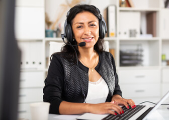 Friendly hispanic female call center operator receiving calls and using laptop in office