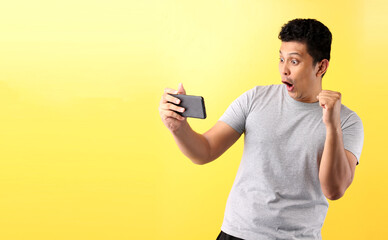 Asian man fun addicted to play mobile game on yellow background in studio With copy space.