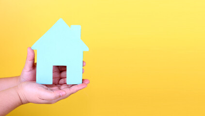 Fototapeta na wymiar Adult hands holding paper house, family home and real estate concept on yellow background in studio.