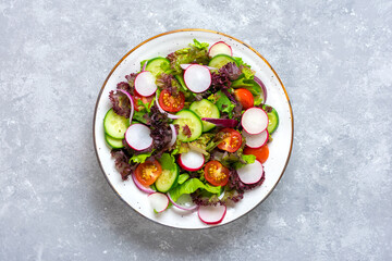 Healthy vegetable salad of cherry tomatoes, cucumber slices, green and purple lettuce leaves, onions and olive oil in plate on concrete table Top view Flat lay Diet, mediterranean menu Vegan food