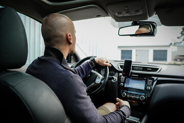 Young handsome short-haired business man sits behind the wheel of his car and drive to home.