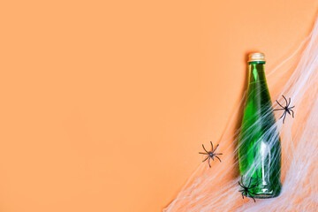 glass bottle with green drink on orange halloween background with spiders , copy space