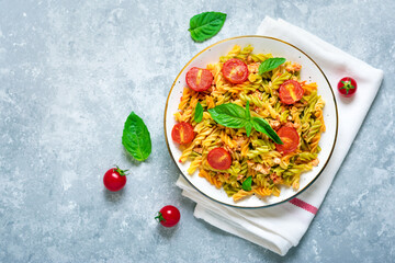 Fusilli - classic italian pasta from durum wheat with chicken meat, tomatoes cherry, basil in tomato sauce in white bowl on gray concrete table Mediterranean cuisine Top view Flat lay