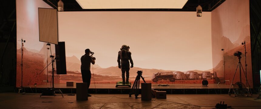 Behind the scenes shot of virtual production stage with huge LED screens, cinematorgapher shooting Mars scene. Future of movie production