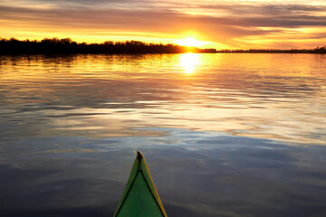 Bow of green kayak at colorful sunset over Danube river at autumn time