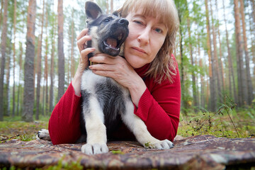 A girl in a red sweater playing with a small German shepherd puppy in the woods